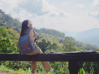 Asian woman with a backpack travels solo on a tropical mountain peak on a sunny summer day. chubby girl with glasses who enjoys and has fun with the outdoor lifestyle.