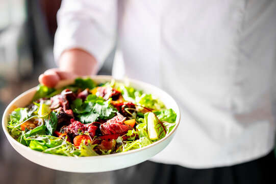 Men's chef or waiter hands hold a Roastbeef salad with vegetables on plate