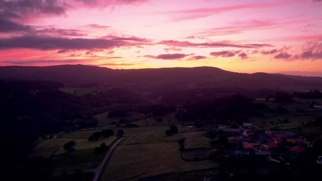 Aerial video of a village and trees in the mountains during pink sunset