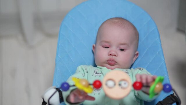 Newborn baby swings in a chaise longue and looks at hanging toys