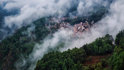 Aerial view of houses nestled among green trees on a mountain slope on a foggy day