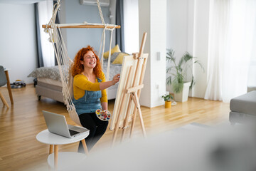 Young, creative woman, sitting in the bright, modern apartment and painting. Beautiful woman...