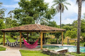 Hammock is suspended between two trees in a garden, next to a small, rectangular swimming pool