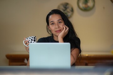 the woman is sitting in front of her laptop smiling with a coffee mug