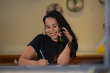 a beautiful woman talking on her cell phone while writing and smiling
