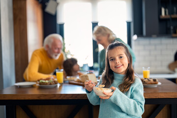 Portrait photo of adorable small girl eating corn flakes with milk in the morning for breakfast...
