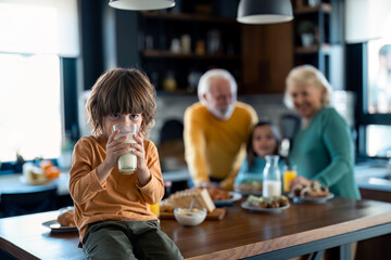 Portrait of a cute boy drinking milk from a glass while sitting on the table during breakfast with...