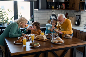 Senior man and woman having breakfast with grandchildren at home. Carefree living, childhood,...