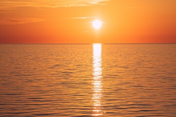 Obraz premium Stunning evening sky colored in a warm orange hue hovers over a serene ocean surface