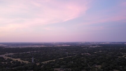 Fototapeta premium Aerial view of houses and roads on green hills at purple sunset