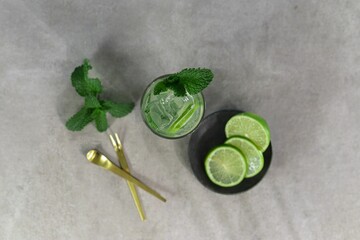 Top view of a glass of mojito with lime and mint leaves on a gray table