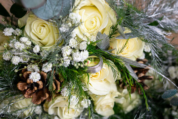 Winter Wedding Splendor: A Diamond Ring Nestled Amongst Lush Yellow Roses and Pine Cones in a Bridal Bouquet