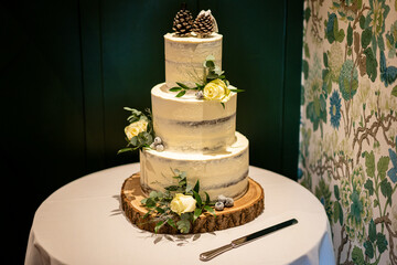 Elegant Three-Tier Rustic Wedding Cake with Pine Cones and Yellow Roses on a Wooden Stand