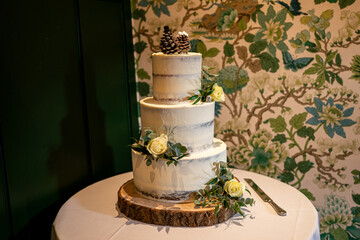 Elegant Three-Tier Rustic Wedding Cake with Pine Cones and Yellow Roses on a Wooden Stand