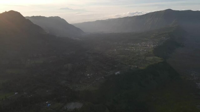 Aerial view of green hills with rural countryside houses with mountains at sunset in Indonesia