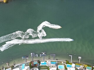 Aerial shot of the boats driving on the coast near luxurious waterfront with swimming pools