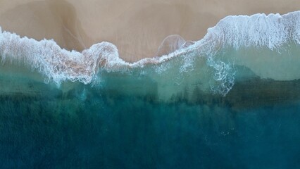 Aerial view of sea waves crashing against a beach in the daylight - obrazy, fototapety, plakaty