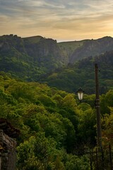 Vertical of a streetlamp against a mountain range covered with a green forest at sunset