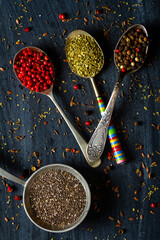 Old metal spoons with different herbs and spices on black background