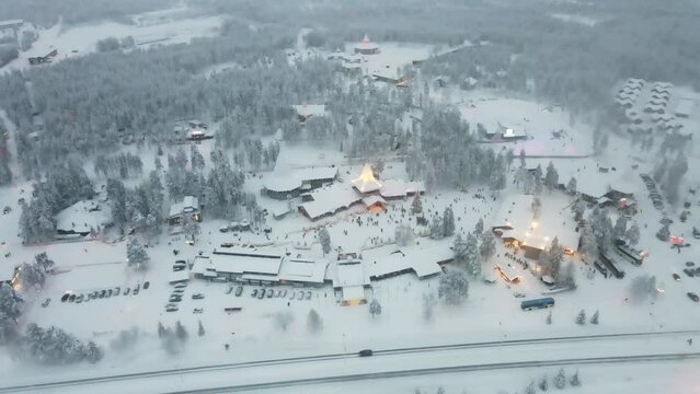 Aerial view of winter snowy forest trees and houses by cars driving in Levi village, Finland