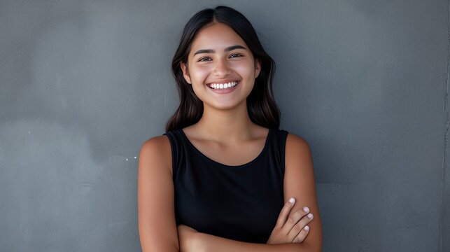 Portrait of a young latin woman with pleasant smile and crossed arms isolated on grey wall with copy space. Beautiful girl with folded arms looking at camera against grey wall - generative ai