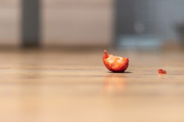 Red strawberry lying on the floor with a bite taken out of it