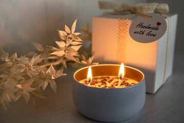 Lit candle and flowers with a handmade gift in a box atop a wooden table