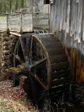 Closeup side view of an old wooden water wheel in motion, with the water running off of it