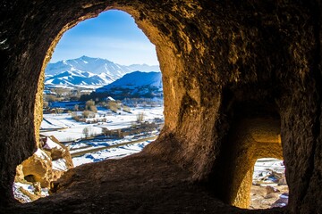 an open, rocky cave door leads to the view of the snowy mountain