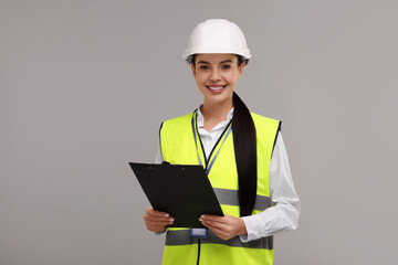Engineer in hard hat holding clipboard on grey background