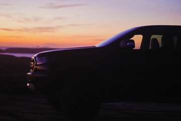 Rear view of a black pickup truck parked on the sand of a beach shoreline at sunset © Wirestock