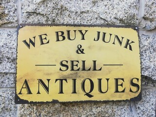 a sign that says we buy junk and sell antiques on a stone wall