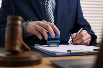 Notary with pen stamping document at table in office, closeup