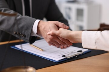 Fototapeta premium Notary shaking hands with client at wooden table in office, closeup