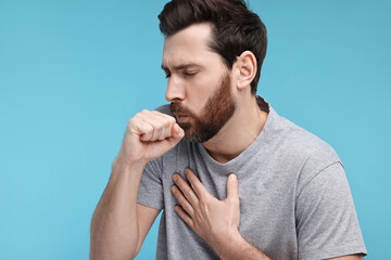 Sick man coughing on light blue background. Cold symptoms