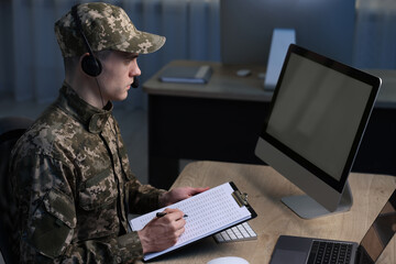 Military service. Soldier with clipboard and headphones working at table in office