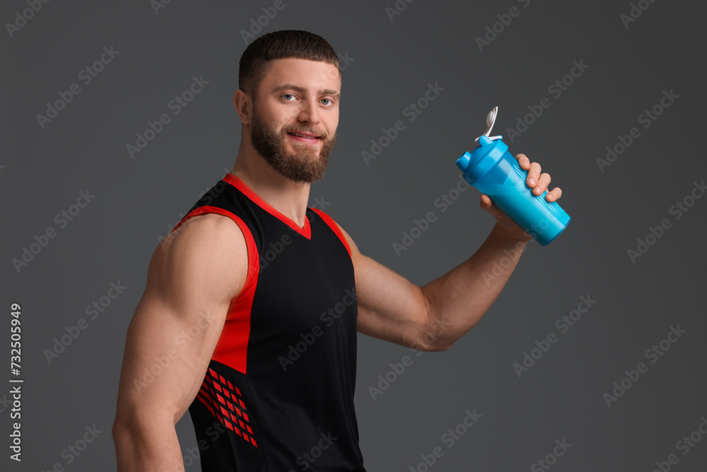 Wall mural Young man with muscular body holding shaker of protein on grey background