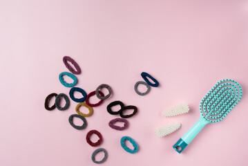 Blue hairbrush with lots of hair ties on a pink background. - obrazy, fototapety, plakaty