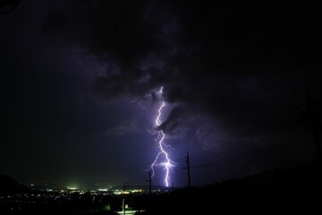 Naklejka premium Night sky illuminated with a dazzling display of purple lightning bolts against a city skyline
