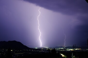 Night sky illuminated with a dazzling display of purple lightning bolts against a city skyline