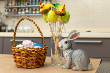 Wicker basket with bunny, tulip, easter colorful eggs on kitchen wooden table. Spring easter composition with space for text.