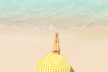 Top view of woman in bikini lying and sunbathes under yellow umbrella on tropical Seychelles sea sand beach. Aerial, drone view - 732511150