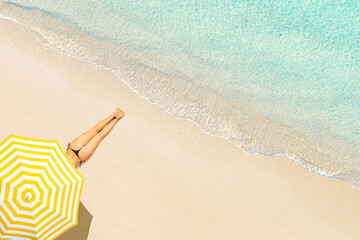 Fototapeta na wymiar Top view of woman in bikini lying and sunbathes under yellow umbrella on tropical Seychelles sea sand beach. Aerial, drone view