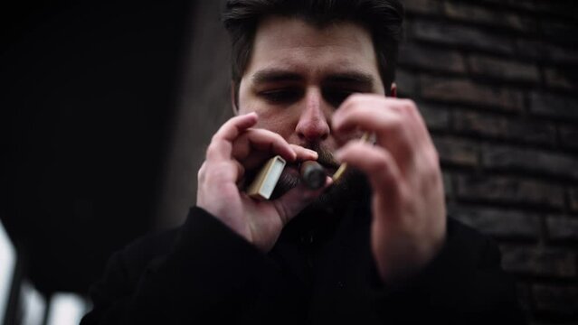 A man in a black coat lighting a cigarette