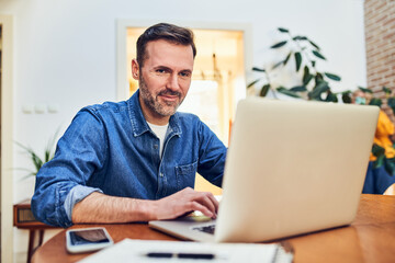 Adult man working remotely at home office using laptop