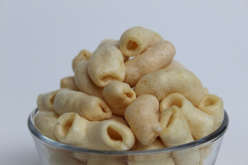 Fried macaroni crackers, on a transparent glass bowl, isolated on white background