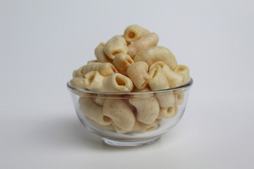Fried macaroni crackers, on a transparent glass bowl, isolated on white background