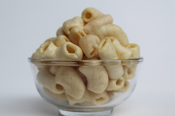 Fried macaroni crackers, on a transparent glass bowl, isolated on white background
