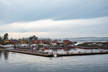 Naklejka premium A wooden Norwegian cottage on the shore of the Oslo fjord on a winter day. Red Norwegian houses