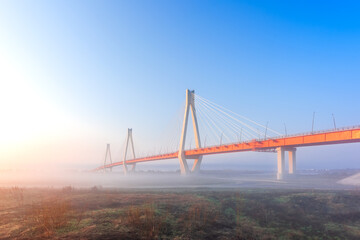 Cable-stayed bridge in fog, in the light of the morning sun and against the background of a clear blue sky. Moore. Russia.